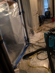 Plastic containment barrier with air scrubber, hoses, and scattered tools during biohazard cleanup setup in a residential hallway in Layton Utah