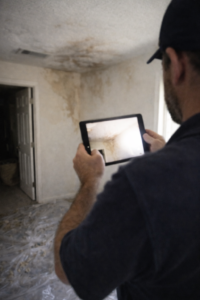 Water damage restoration technician using tablet to document ceiling and wall moisture stains for insurance in a Layton Utah home