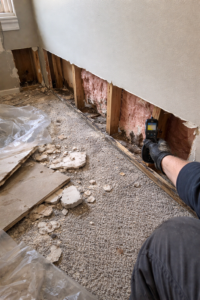 Exposed wall cavity with wet insulation and framing and debris on floor during water damage cleanup in a Layton Utah home